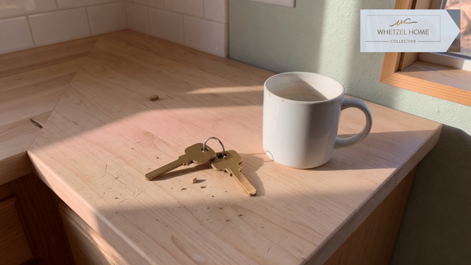 Two brass keys and a white mug on a wood counter
